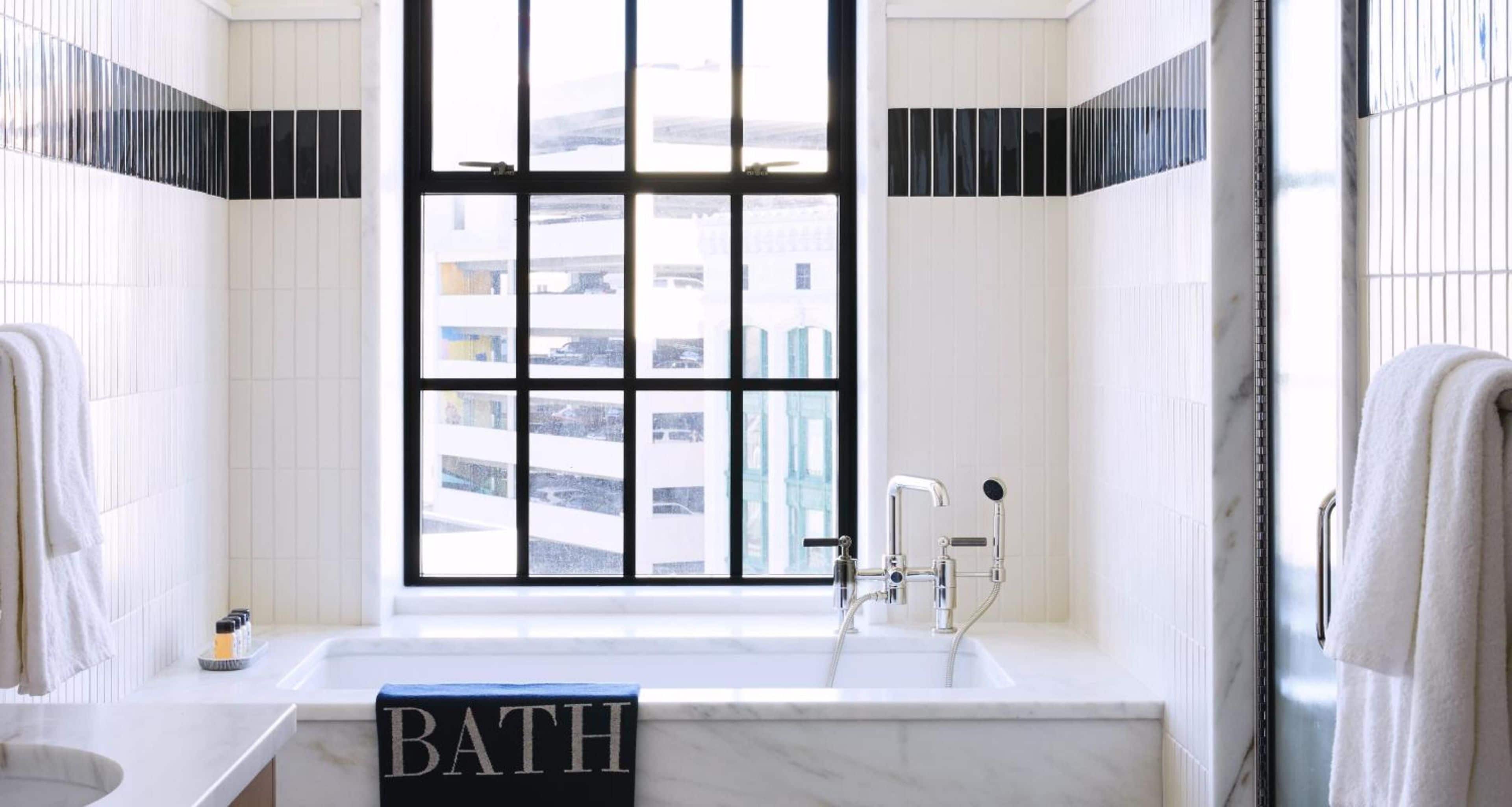 Un baño con bañera, una ventana que ofrece vistas a edificios y un perchero.