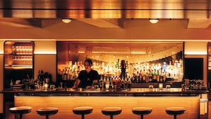 Un espace bar avec un barman, un comptoir bien garni et des tabourets de bar.