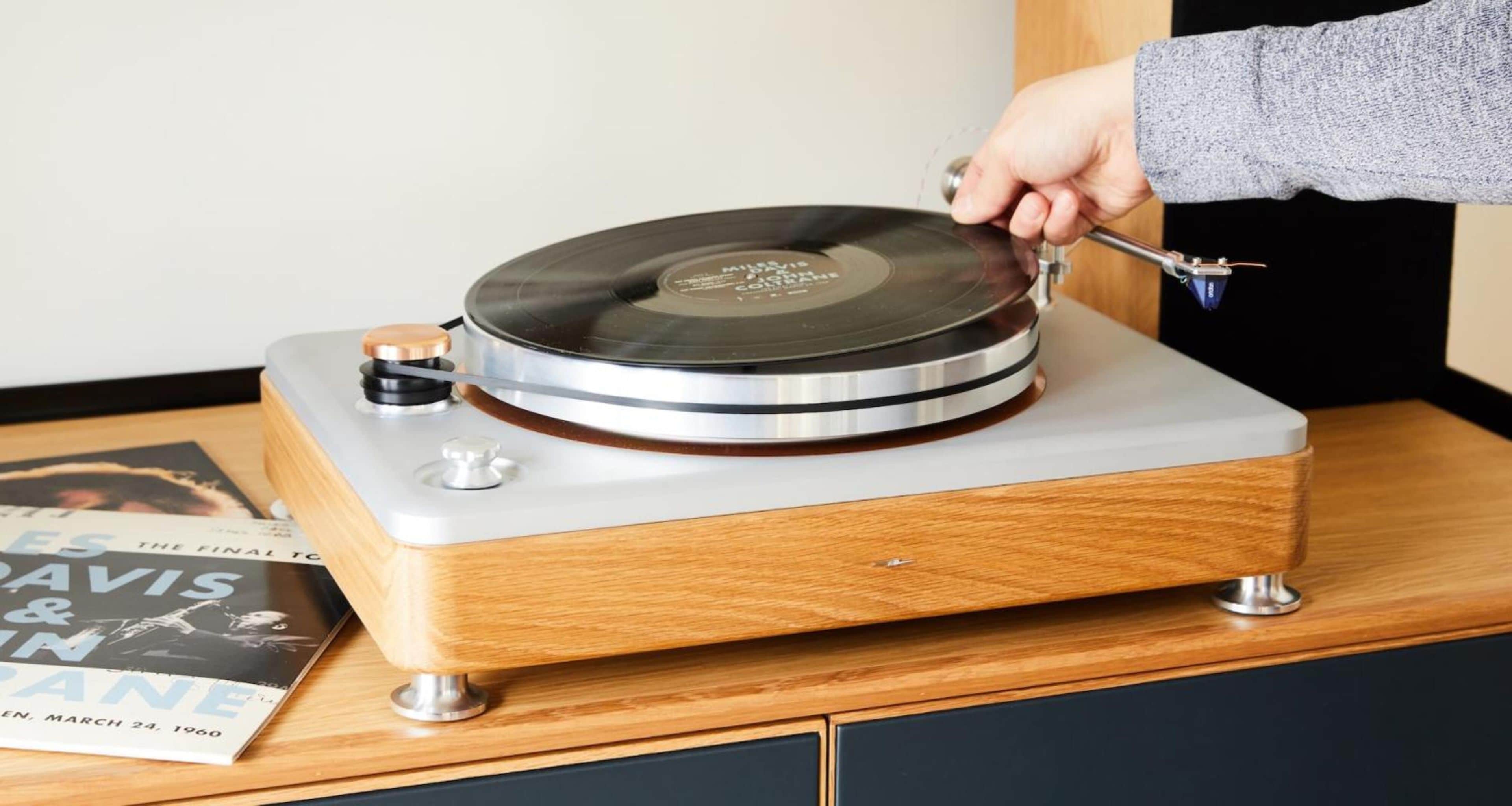 A turntable with a wooden base and metallic accents, placed on a table with a book titled 'The Final Touch' nearby.