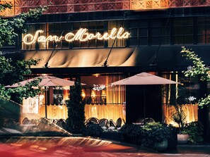 A restaurant with outdoor seating, a neon sign, and a covered patio area. - Shinola Hotel (Detroit)