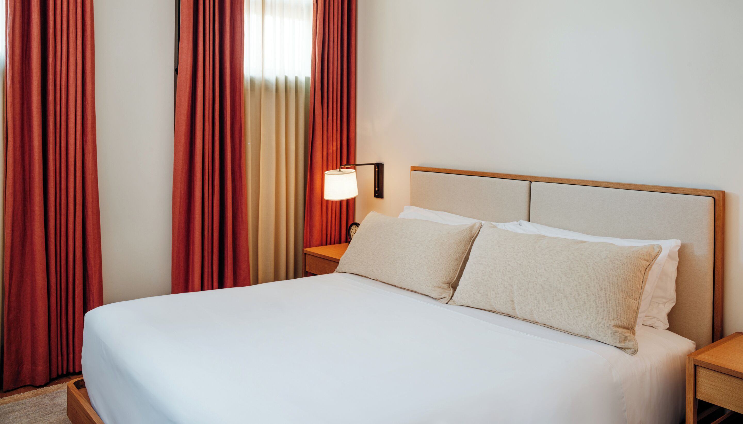 Una cama bien hecha con sábanas blancas, un cabecero de madera y una lámpara de noche.