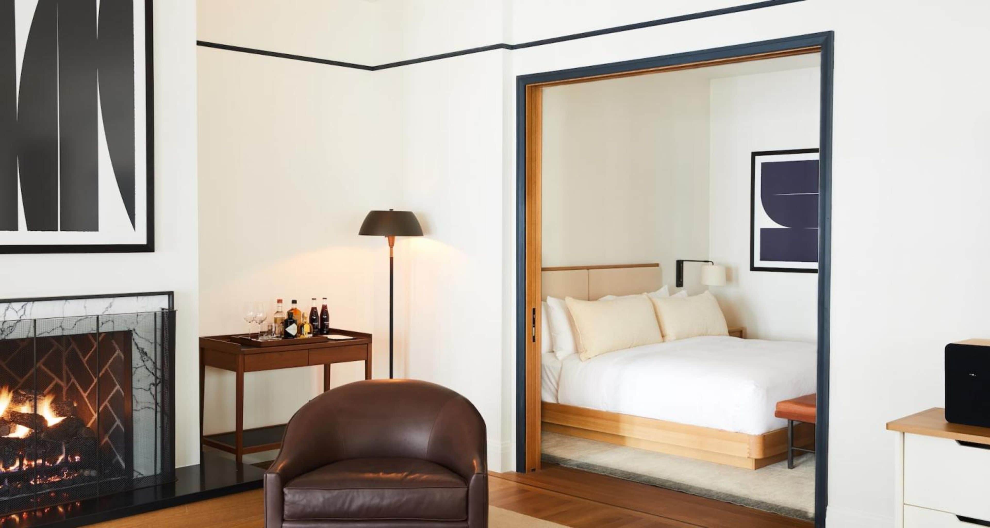 Ein Hotelzimmer mit Kamin, einem Bett mit weißer Bettwäsche, einem braunen Ledersessel und einem Nachttisch mit Lampe.