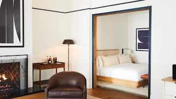Ein Hotelzimmer mit Kamin, einem Bett mit weißer Bettwäsche, einem braunen Ledersessel und einem Nachttisch mit Lampe.