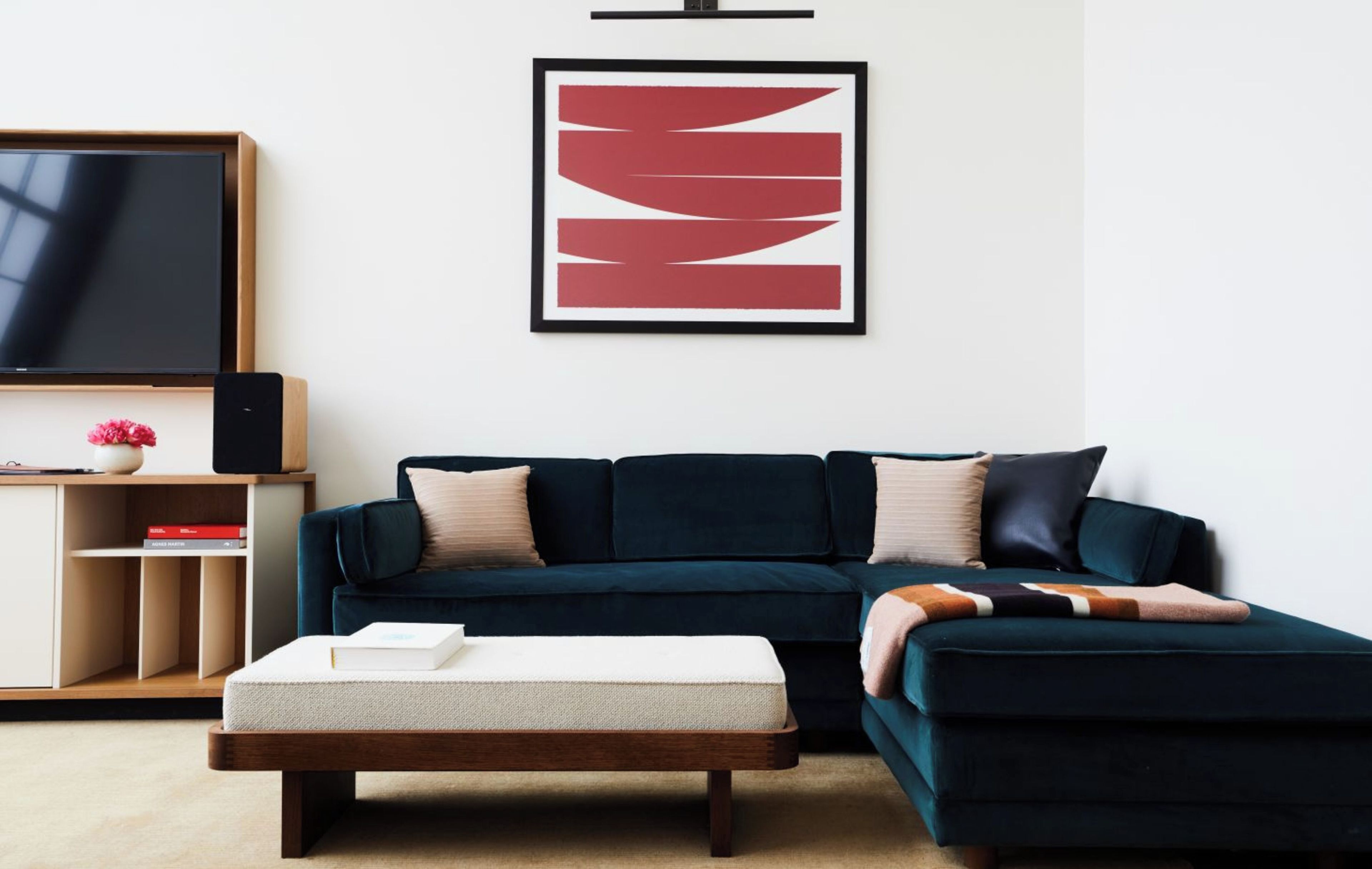 A modern living room with a dark blue sofa, a white ottoman, and a flat-screen TV on a wooden stand.