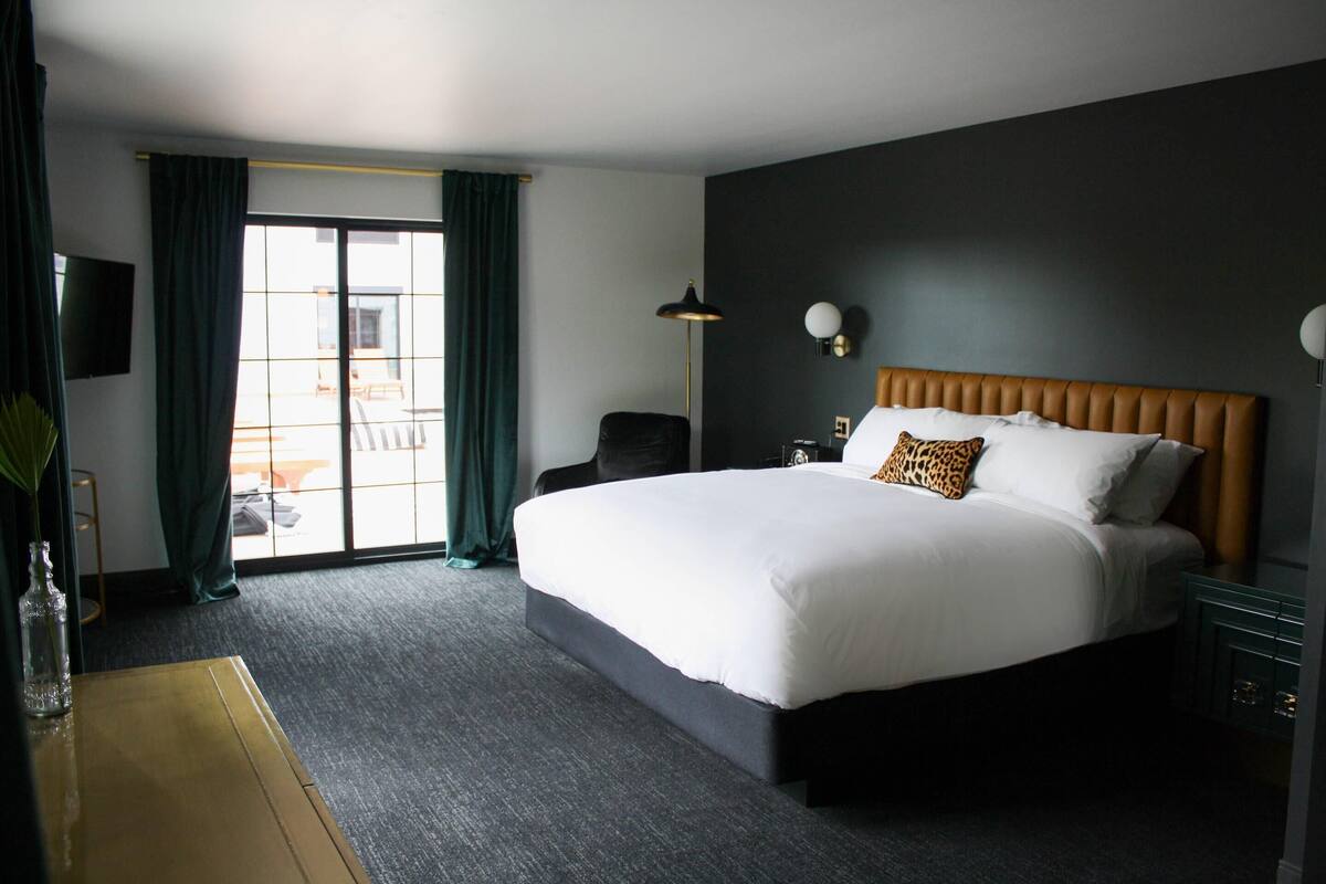 Habitación de hotel con una cama grande, un escritorio, una silla, un televisor y vistas al exterior.