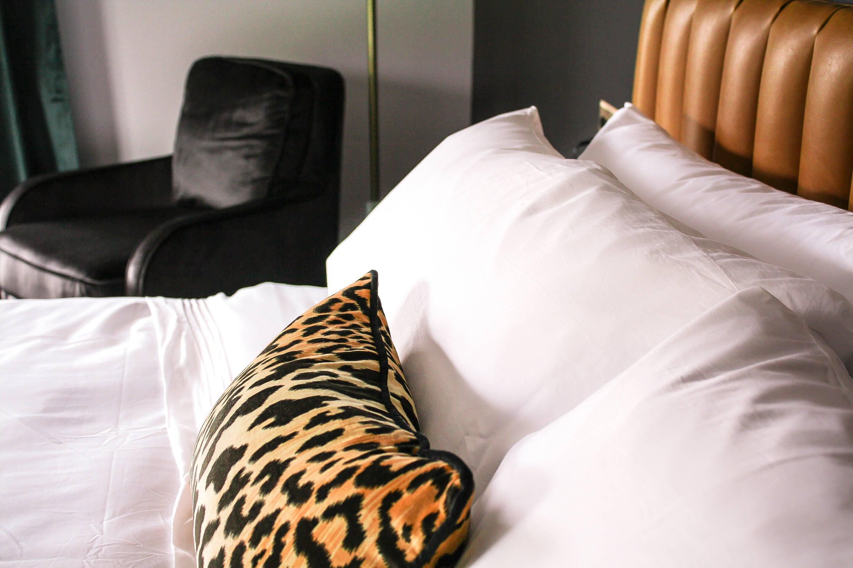 Una cama con sábanas blancas y un cojín estampado de leopardo.