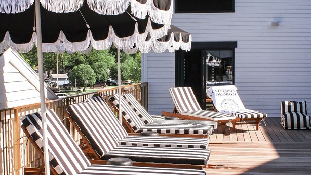 A deck with striped lounge chairs and a sign reading "UNIVERSITAT OKOBOJ". - The Inn Hotel Lake Okoboji, an Ascend Collection Hotel (Arnolds Park)