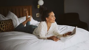 A person lying on a bed with a book, in a room with a wooden headboard and a round wall light. - The Inn Hotel Lake Okoboji, an Ascend Collection Hotel (Arnolds Park)