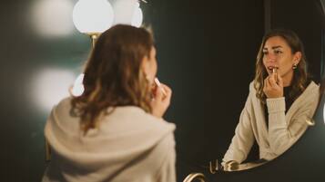 A person in a robe sitting in front of a mirror with a sink and a faucet.