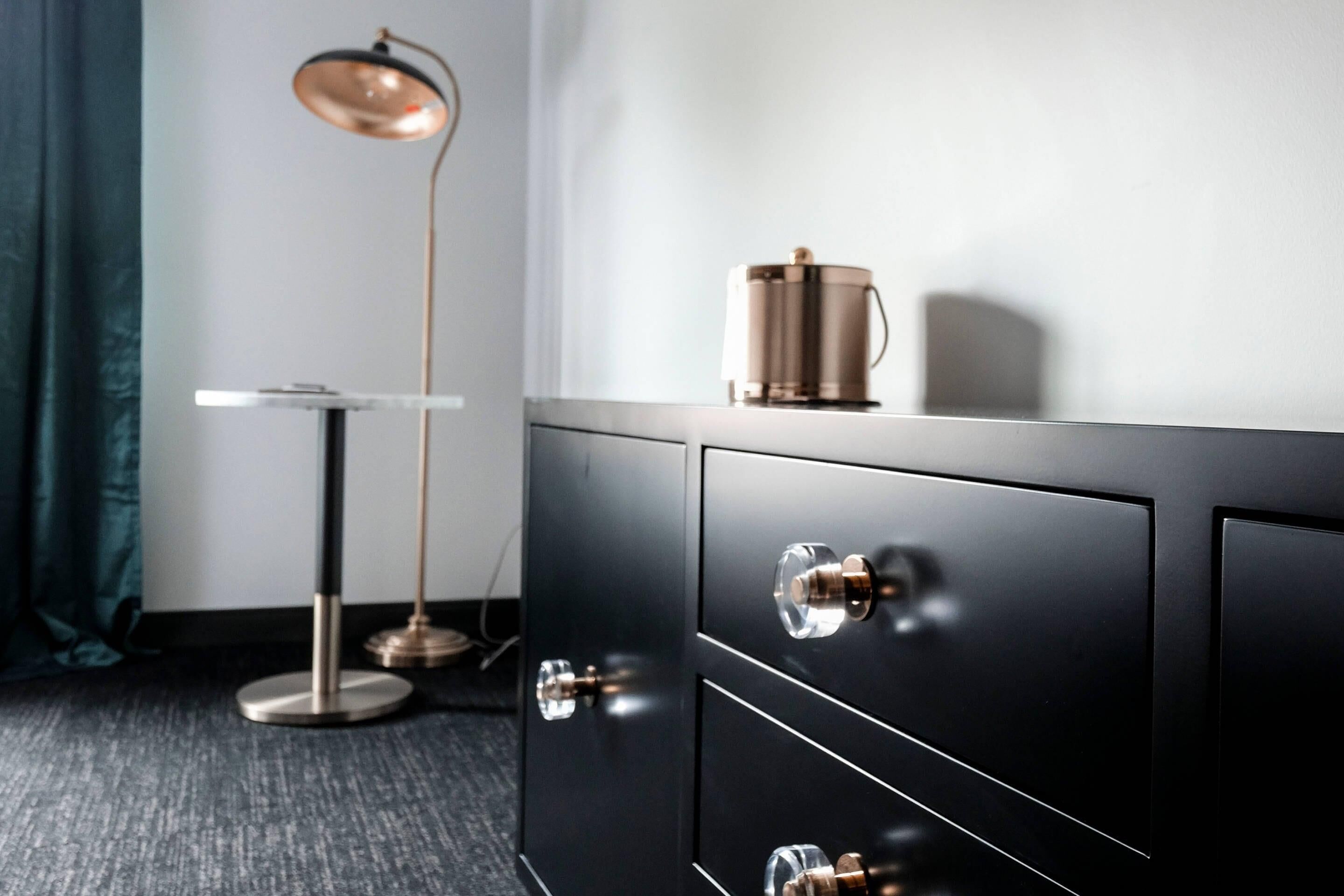 Una habitación moderna con un mueble negro, una lámpara de pie y una cafetera encima.