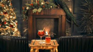 A cozy seating area with a small table featuring two drinks, a decorated Christmas tree, and a fireplace in the background.
