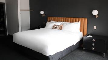 A neatly made bed with white linens and a single leopard print pillow, a wooden headboard, and a black nightstand with drawers.