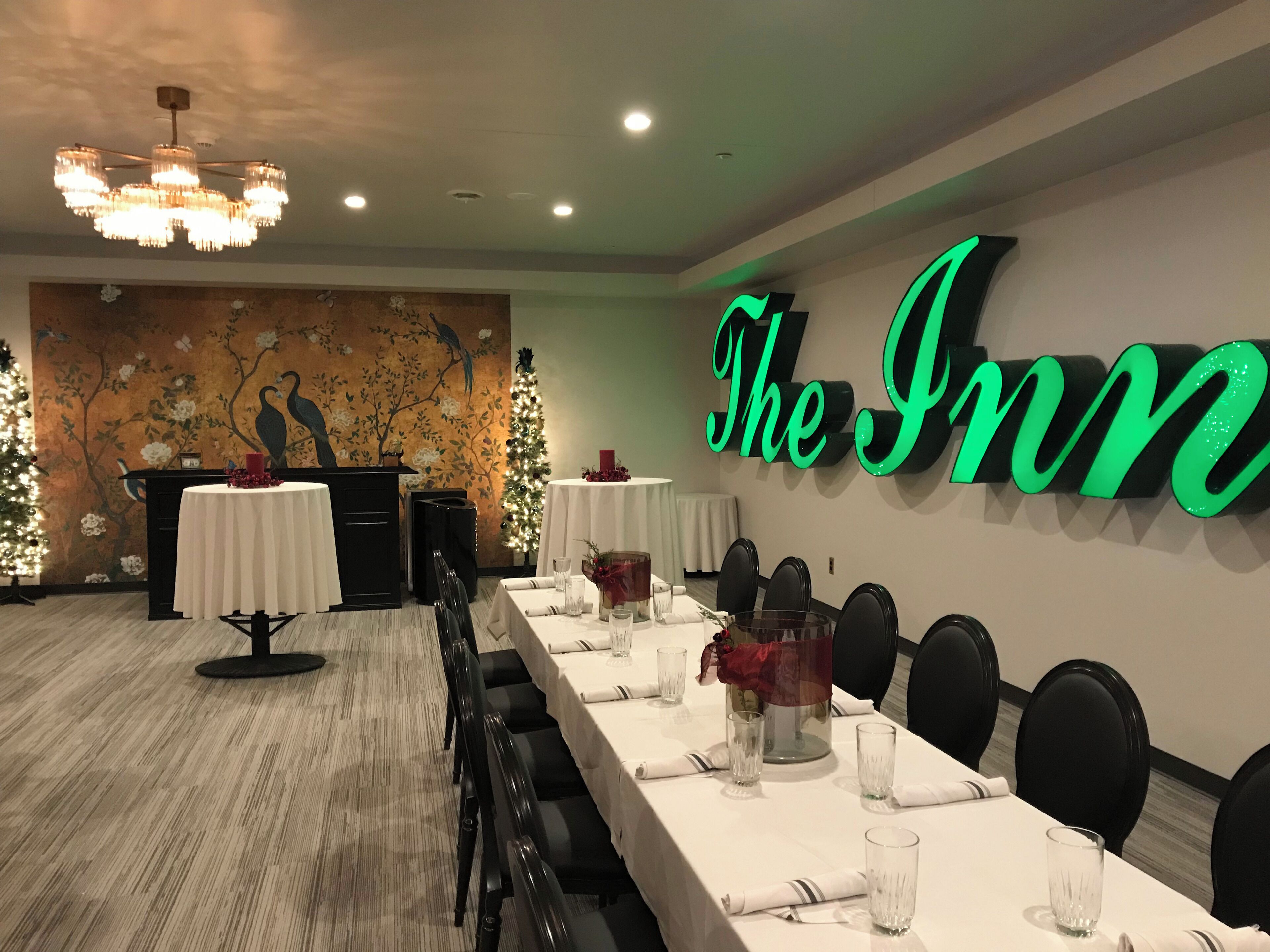 Una sala de conferencias con una larga mesa dispuesta para una reunión, una pared con el letrero iluminado 'The Inn', y un mural con pájaros y flores.