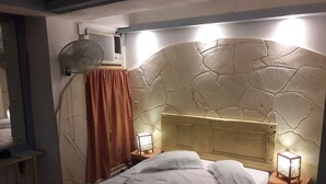 A bedroom with a stone headboard, a bed with white linens, a standing fan, a heater, and a nightstand with a lamp. - B&B El Leon Azul Habana Vieja (Havana)