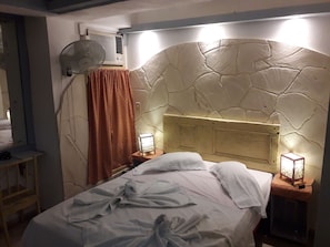 A bedroom with a stone headboard, a bed with white linens, a standing fan, a heater, and a nightstand with a lamp. - B&B El Leon Azul Habana Vieja (Havana)