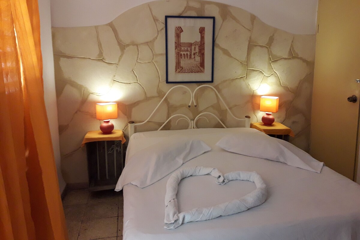 A hotel room with a bed, two bedside lamps, a framed picture on the wall, and a towel on the bed.