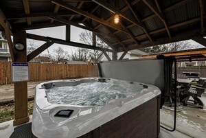 A hot tub under a wooden structure with a safety sign, a clock, and a grill in the background.