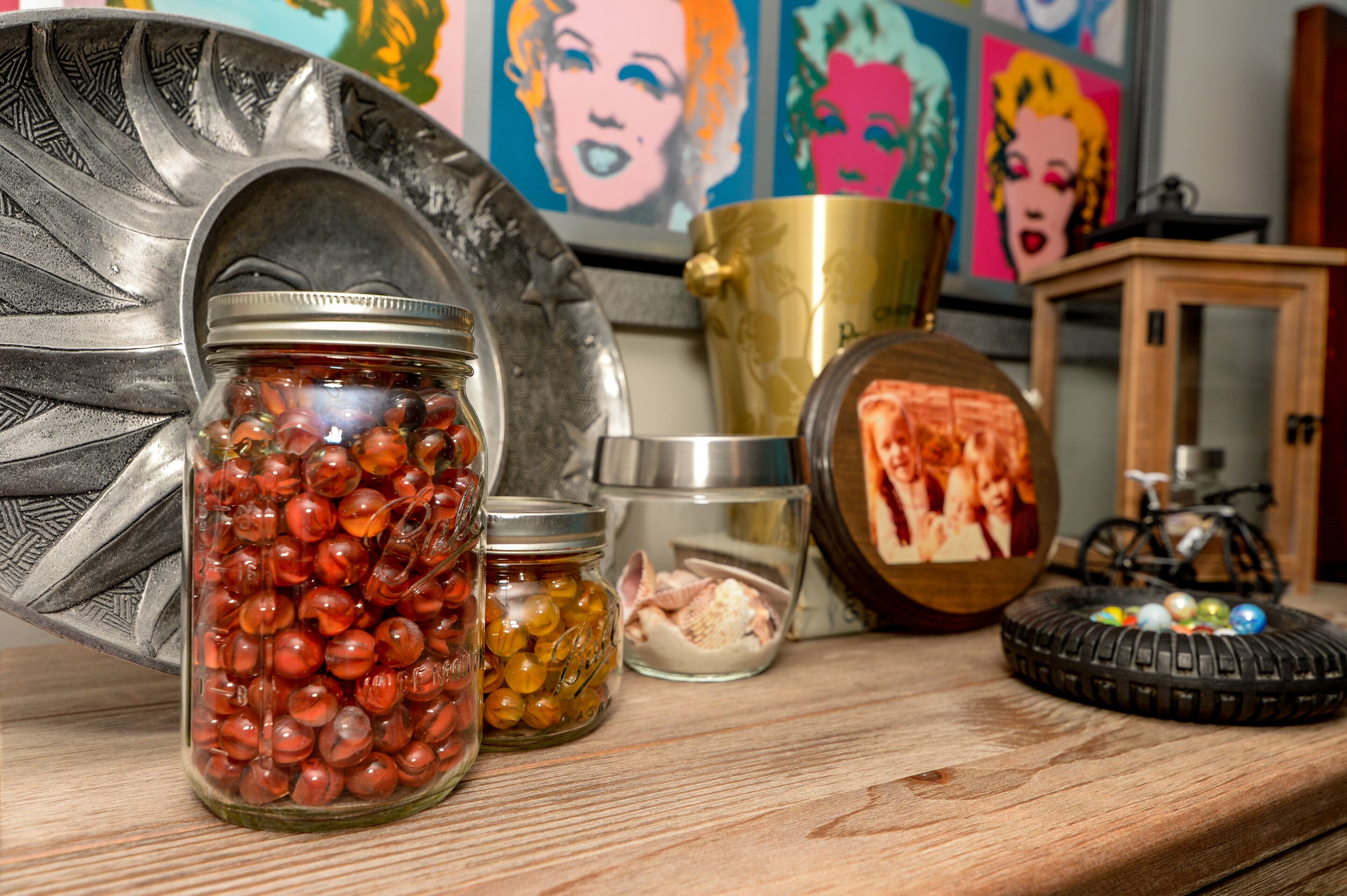 A wooden table with jars of marbles, a brass container, and a bicycle.