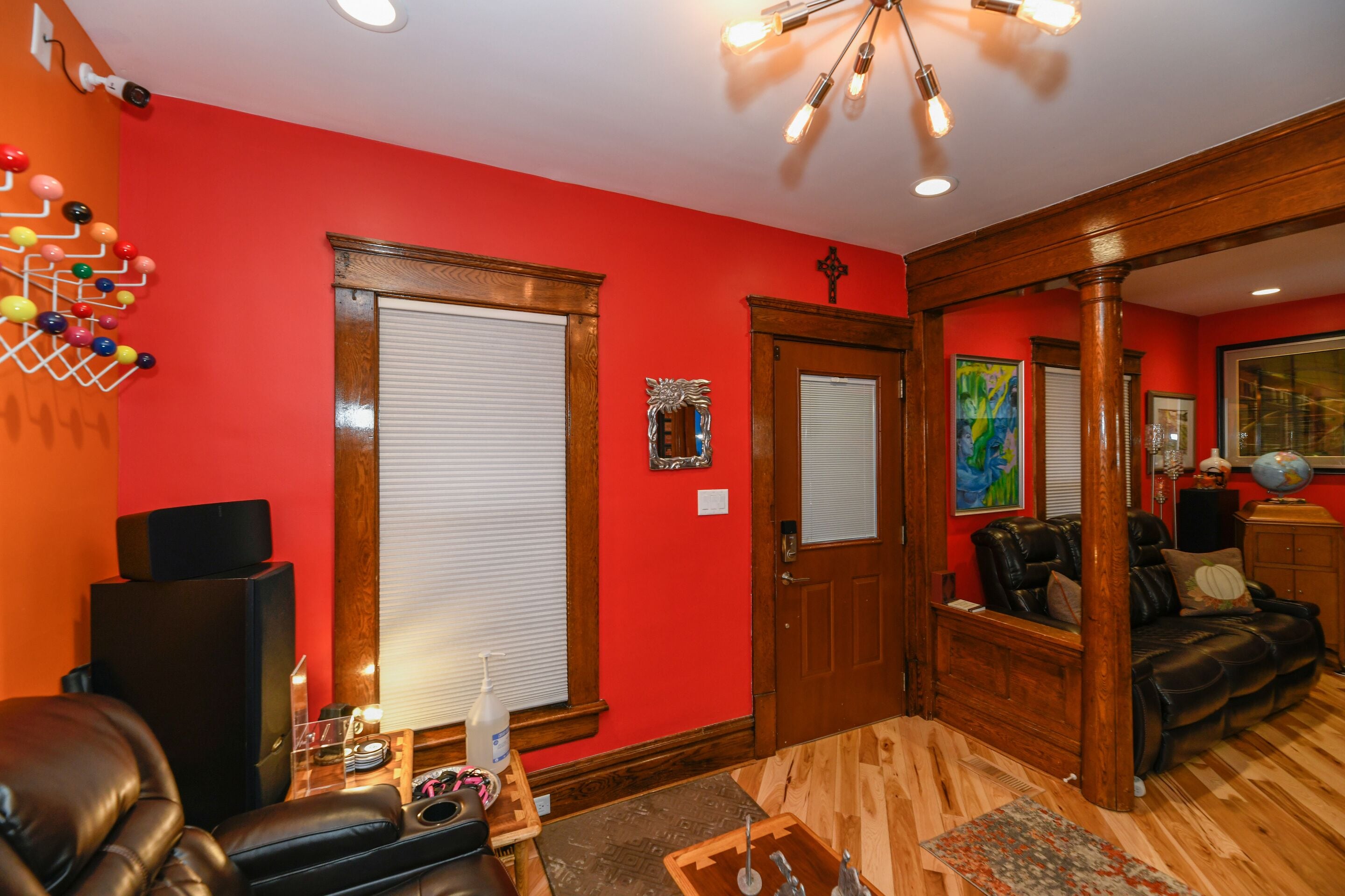 A room with red walls, a wooden floor, a leather sofa, a massage chair, and a wooden door with a mirror.