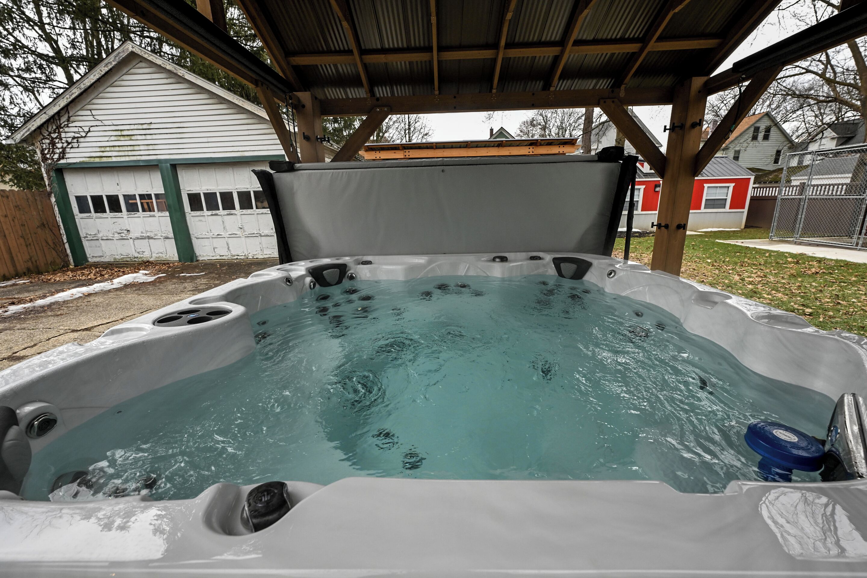 Un bain à remous sous une pergola en bois, avec un garage blanc en arrière-plan.