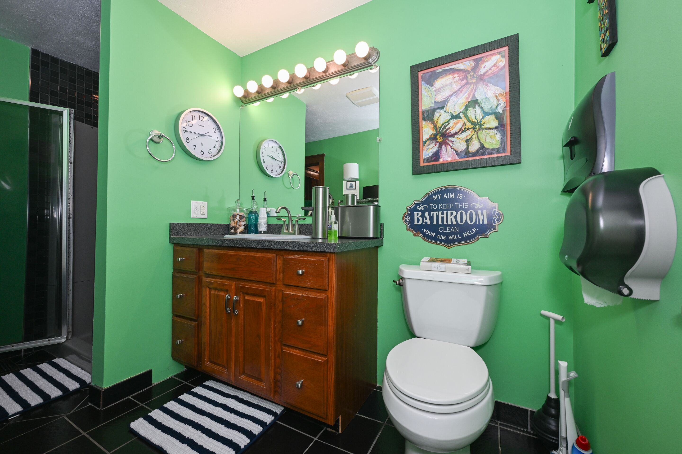 Een badkamer met groene wanden, een houten wastafelmeubel, een wit toilet, een wastafel met spiegel en een handdroger.
