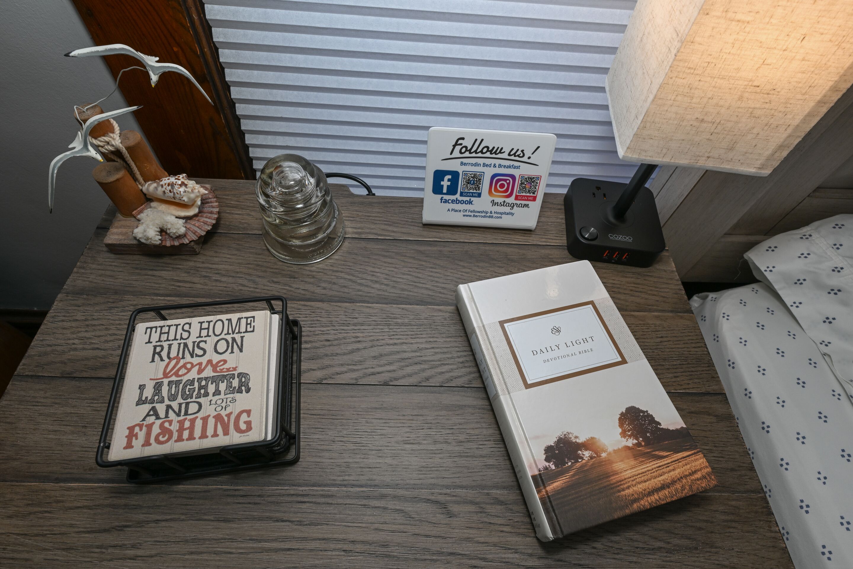 A wooden table with a lamp, a sign, a book, and a decorative item.