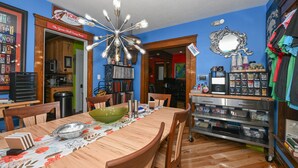 Un comedor con una mesa de madera, sillas y una lámpara decorativa en el techo. Hay una zona de cocina con armarios y un microondas.