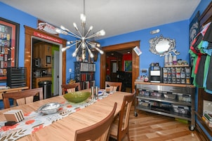 A dining area with a wooden table, chairs, and a decorative ceiling light. There is a kitchen area with cabinets and a microwave.