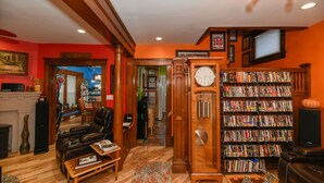 Una sala de estar con chimenea, un reloj y una estantería llena de libros y DVD.