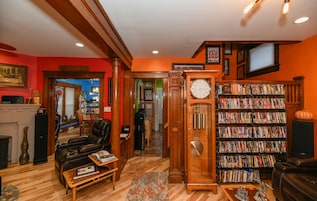 Una sala de estar con chimenea, un reloj y una estantería llena de libros y DVD.