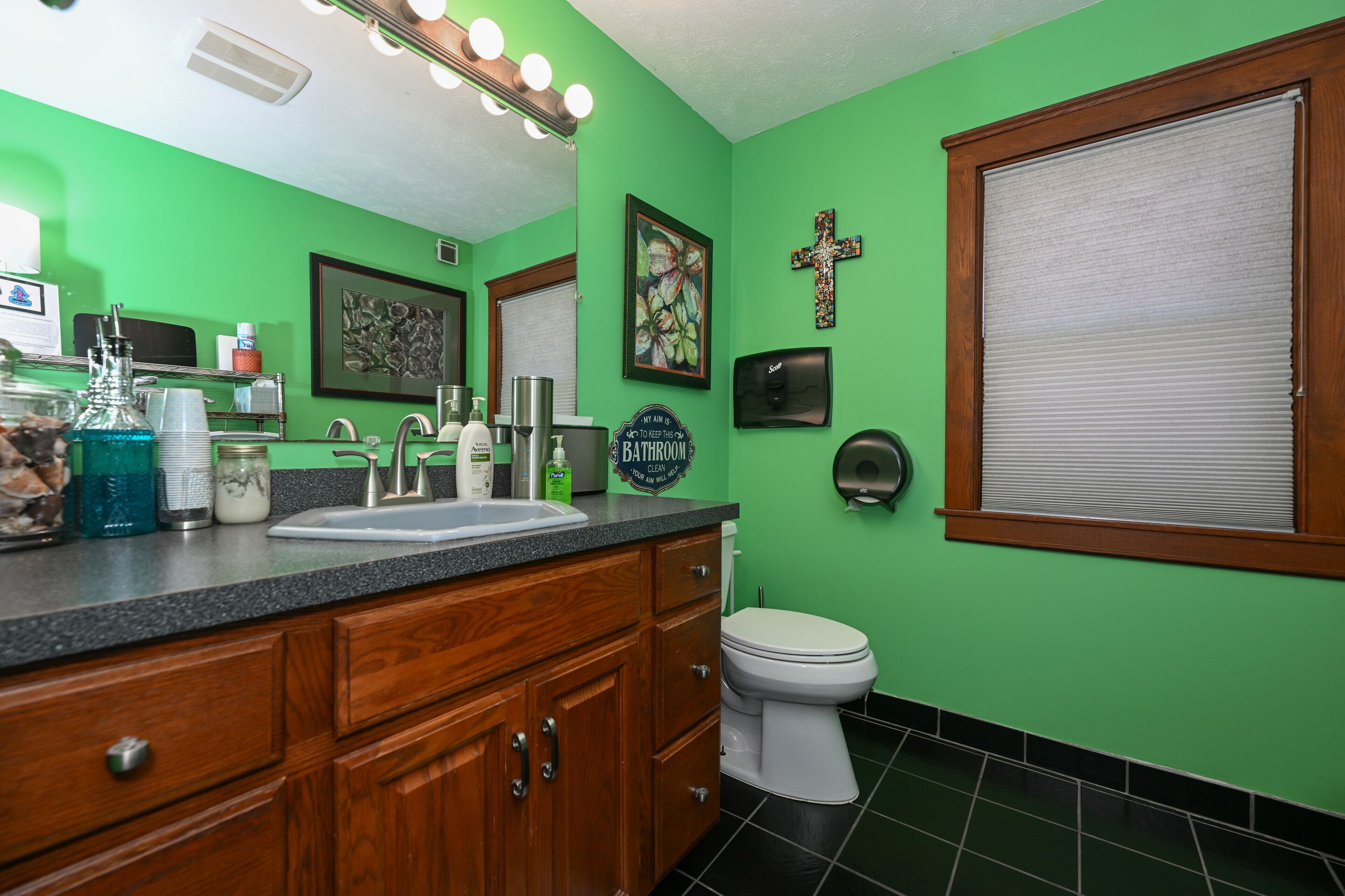 A bathroom with green walls, a wooden vanity, a sink, and a toilet.