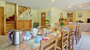 Ein Essbereich mit Holztisch, gedecktem Tisch für eine Mahlzeit, einer Treppe und einem Bücherregal mit Büchern und Dekorationsobjekten.