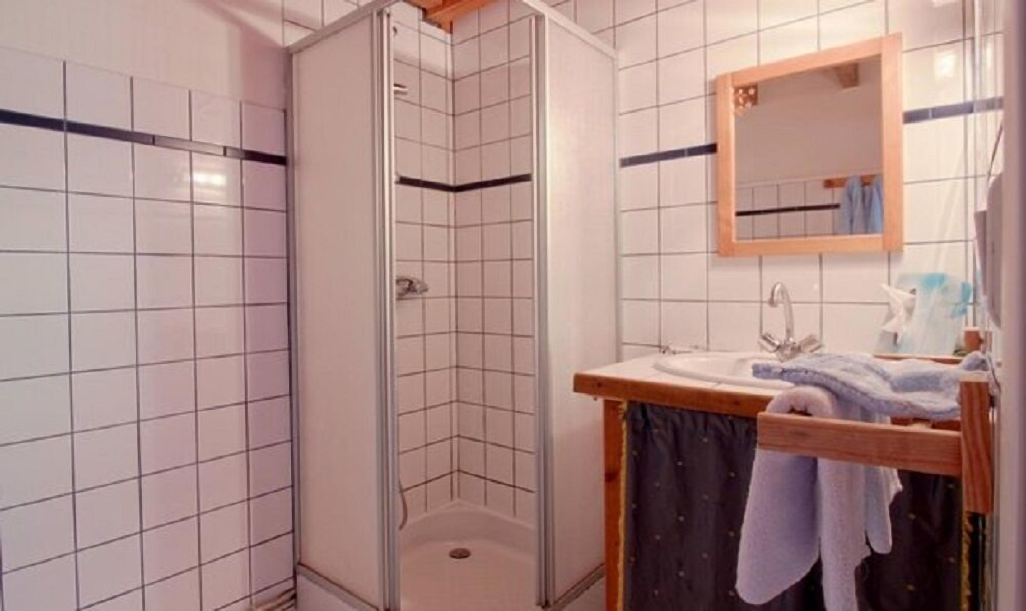 A bathroom with white tiled walls, a shower with a glass door, a sink with a wooden countertop, and a mirror above the sink.