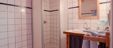 A bathroom with white tiled walls, a shower with a glass door, a sink with a wooden countertop, and a mirror above the sink.