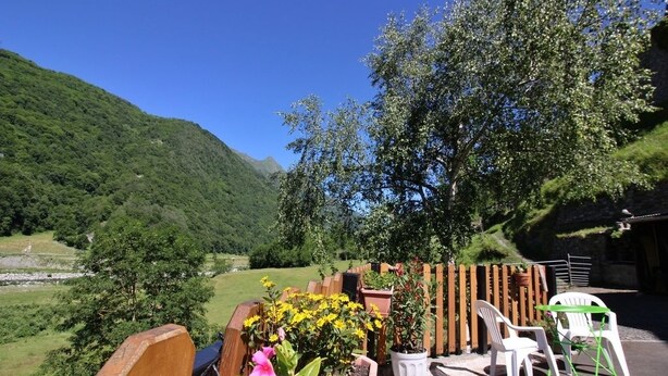 Eine Terrasse mit Sitzgelegenheit, einem Holzzaun und Blick auf ein grünes Tal und Berge.
