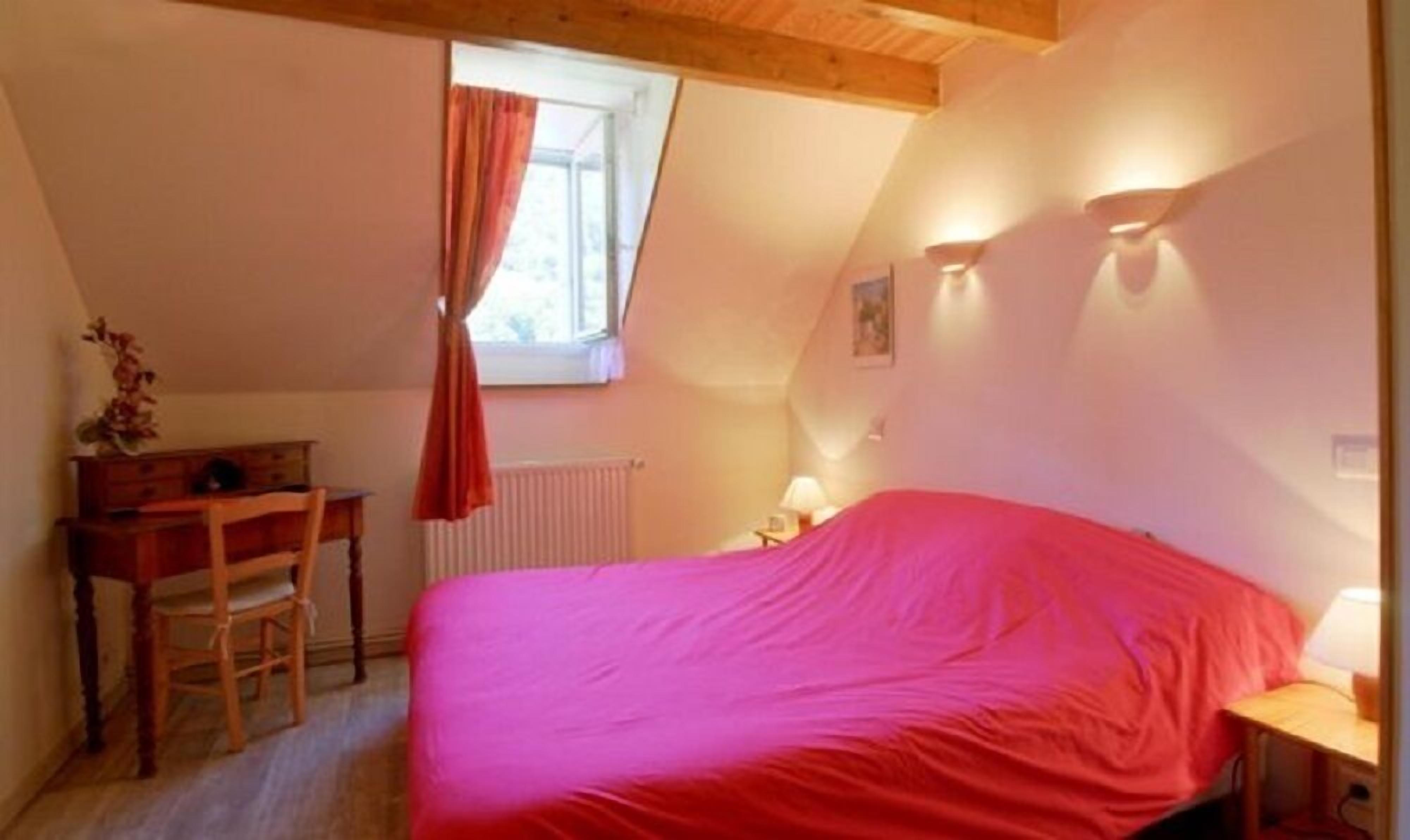 A bedroom with a bed, a desk, a chair, a window with curtains, and a radiator.