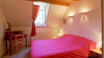 A bedroom with a bed, a desk, a chair, a window with curtains, and a radiator.