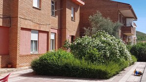 Ein zweistöckiges Backsteingebäude mit Balkonen, einem gepflasterten Innenhof und üppigem Grünwerk.
