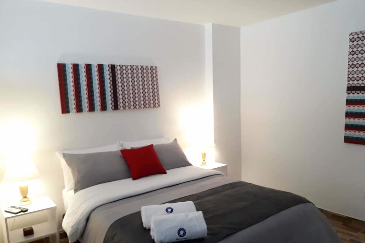 A hotel room with a bed, two bedside tables, a lamp, and a wall with patterned artwork.