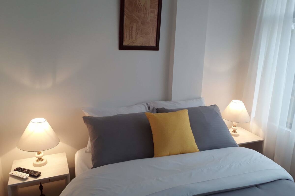 A hotel room with a bed, two bedside lamps, a remote control, and a framed picture on the wall.
