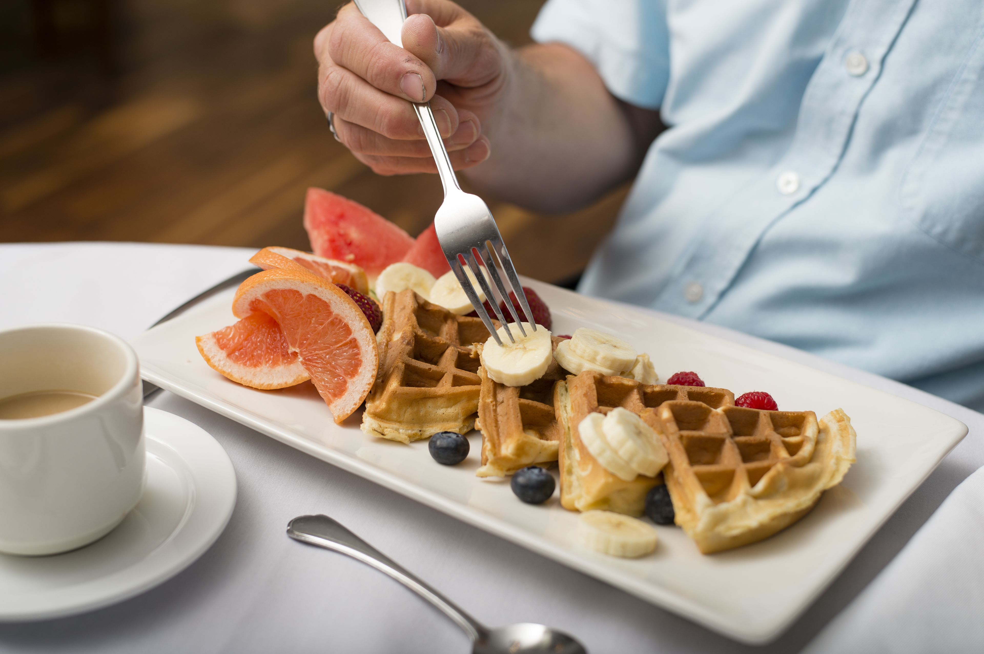 A plate of waffles topped with fruit and a cup of coffee on a table.