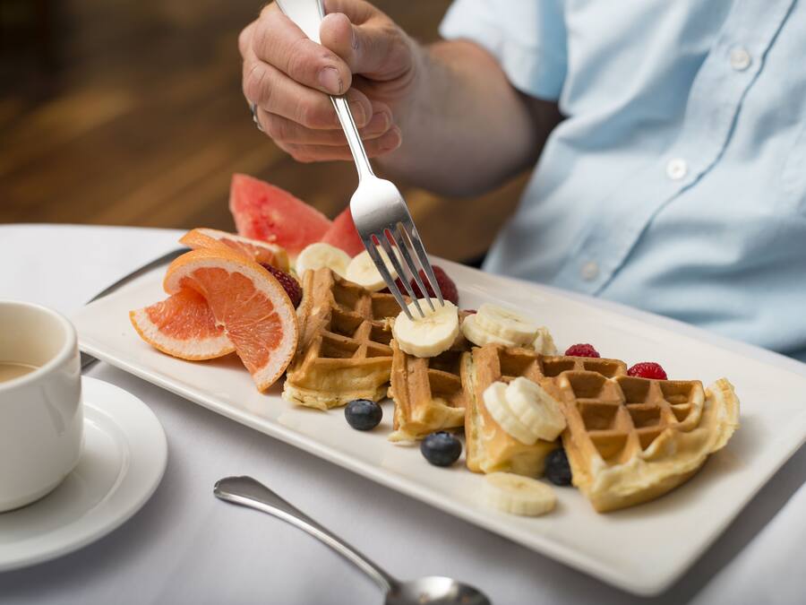 A plate of waffles topped with fruit and a cup of coffee on a table.