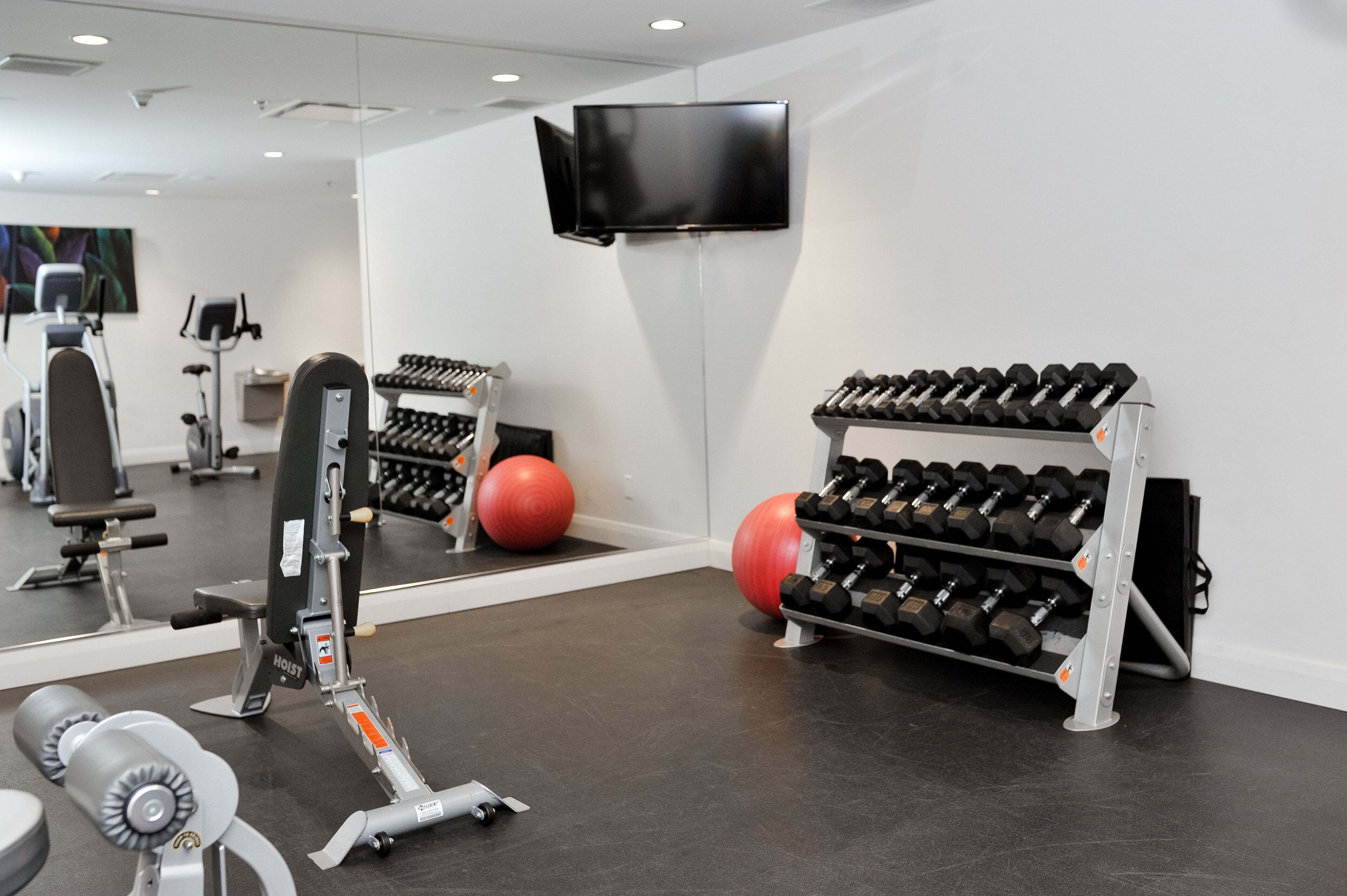 Ein Fitnessraum mit Trainingsgeräten, einem Fernseher und einem Spiegel.