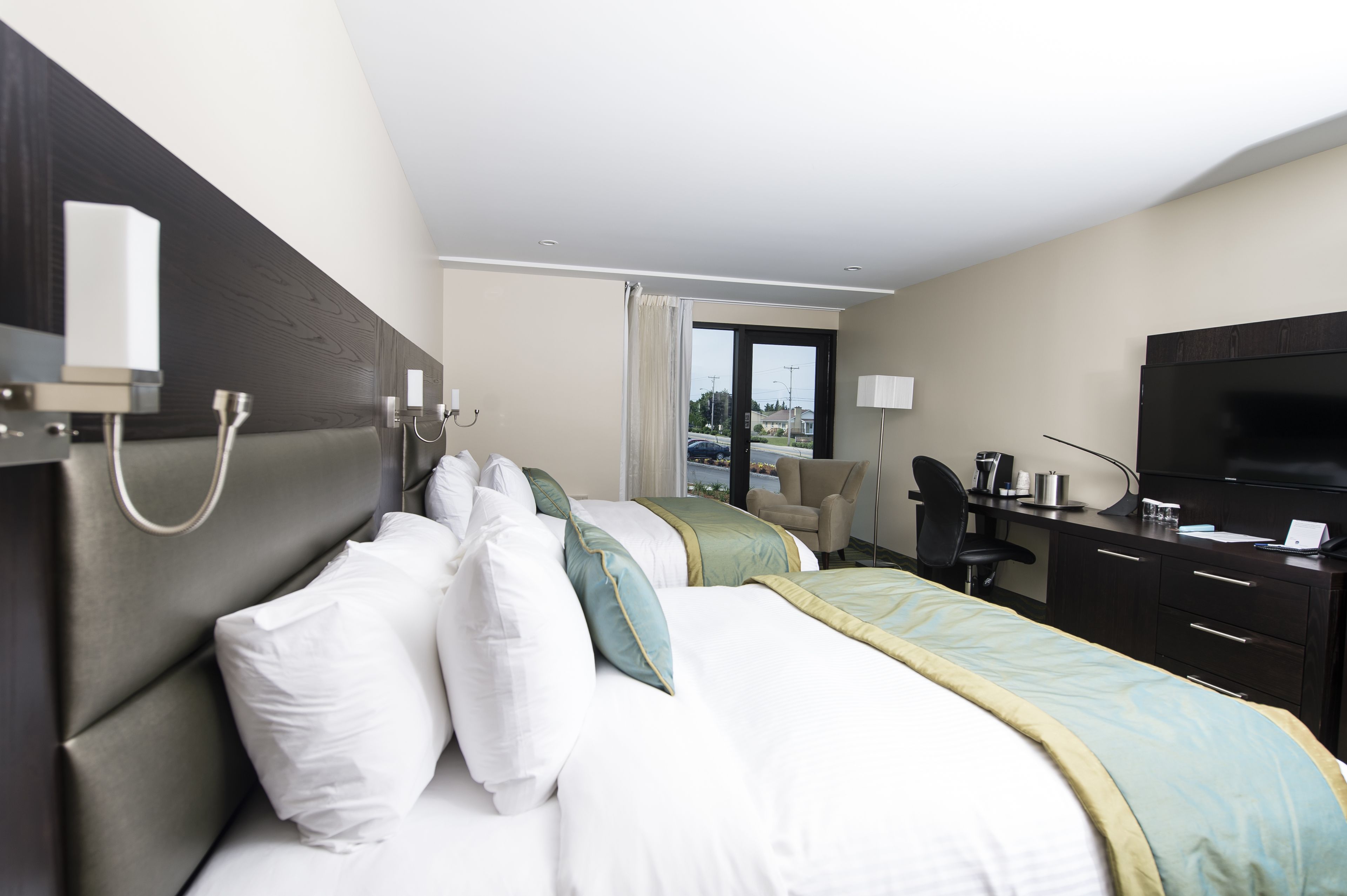 A hotel room with a bed, a desk, a chair, a television, and a window with a view of the outside.