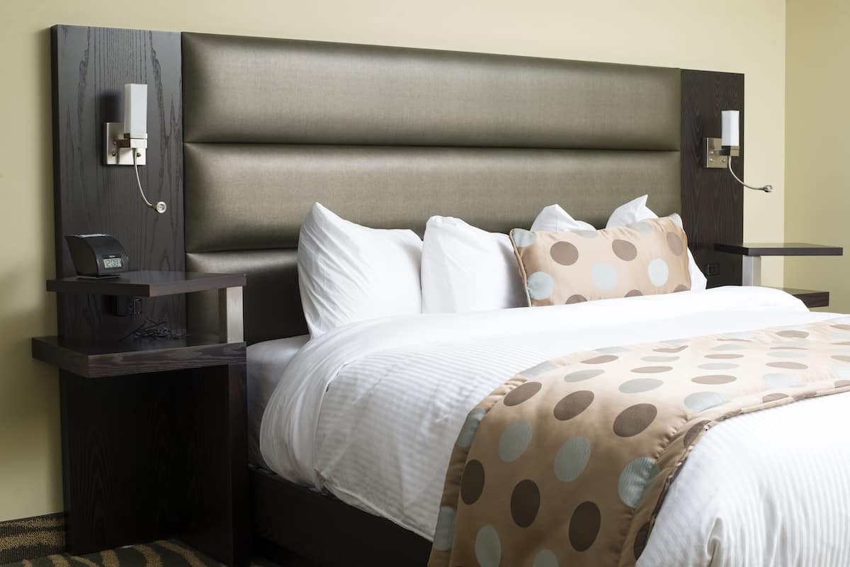 A hotel room with a large bed, a bedside table with a clock, and a wall-mounted light fixture.