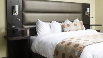 Una habitación de hotel con una cama grande, una mesita de noche con un reloj y una lámpara fijada a la pared.
