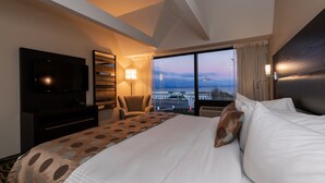Habitación de hotel con una cama grande, televisión, escritorio y vista a la ciudad por la ventana.