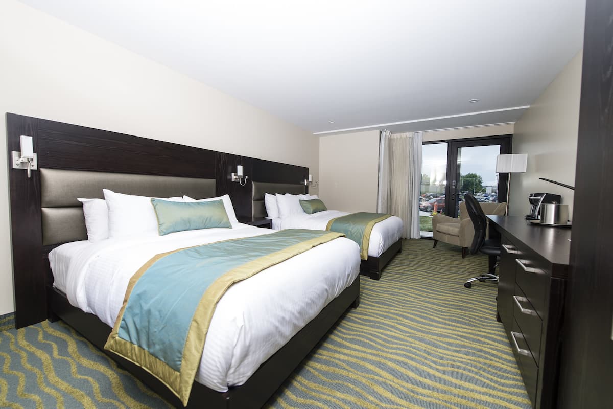 A hotel room with two beds, a desk, a chair, and a view of the parking area.