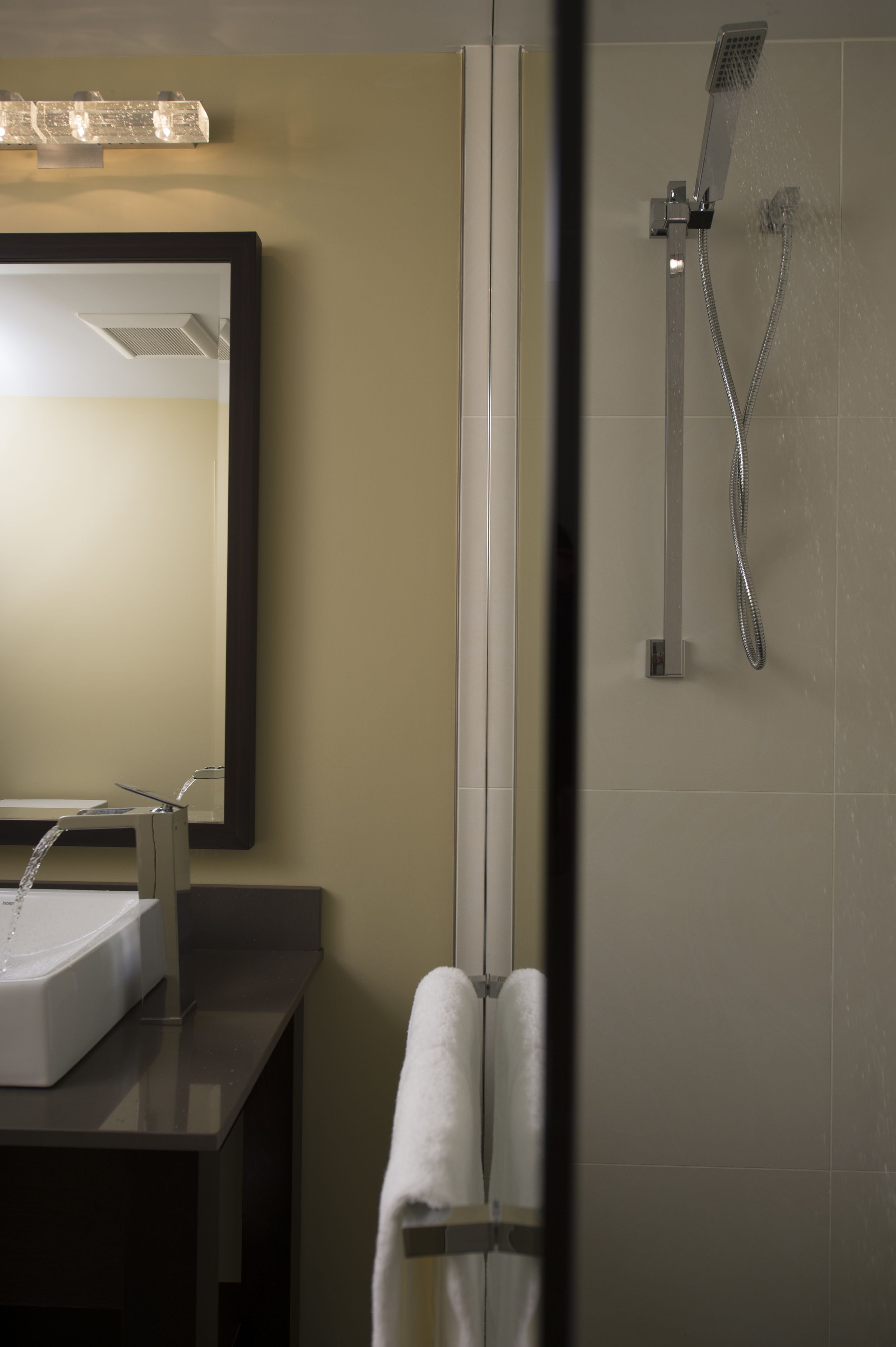 A modern bathroom with a large mirror, a sink, and a shower with a handheld showerhead.