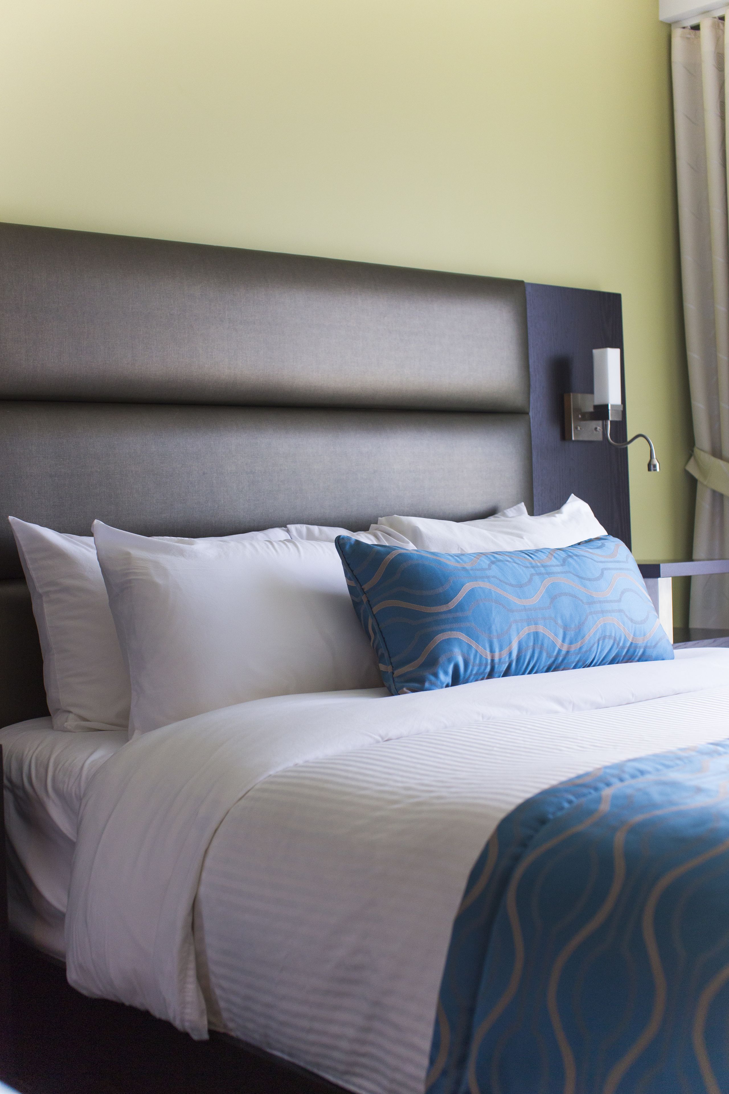 A neatly made bed with white and blue bedding, a headboard, and a wall-mounted light fixture.
